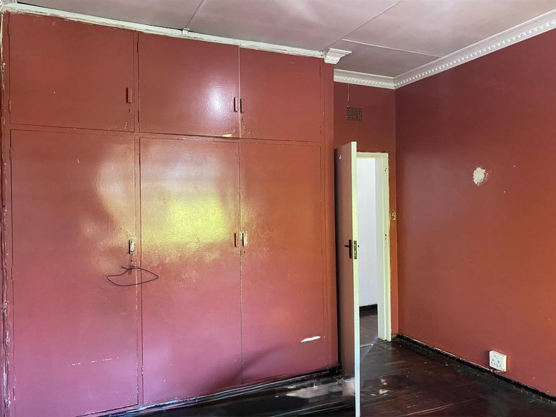 An empty bedroom featuring built-in cupboards, crown molding, and dark timber flooring, requiring cosmetic updates to the walls and floor finishes.