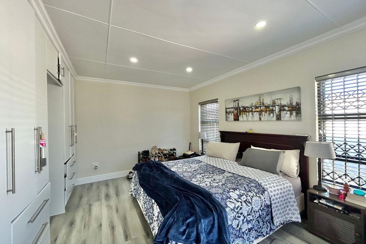 A well-maintained bedroom featuring built-in white cabinetry, modern wood-look flooring, recessed ceiling lighting, and security shutters on the windows.