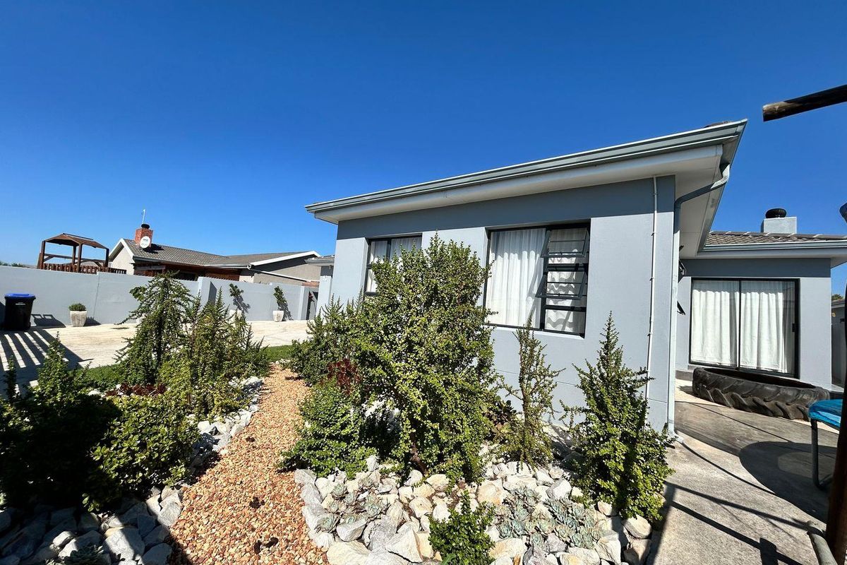 A well-maintained rear exterior view of the house featuring a landscaped garden with gravel pathways, rockery, and modern grey painted exterior walls.