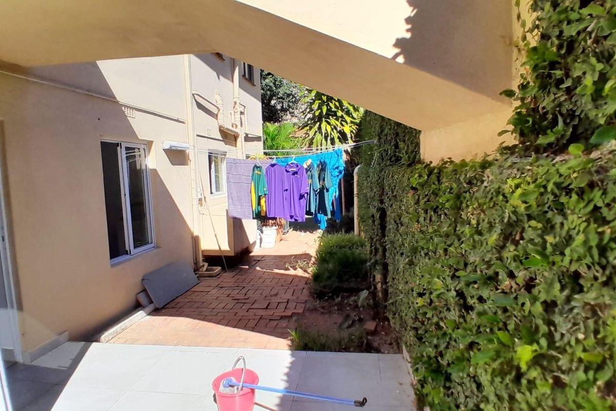 A private outdoor courtyard area featuring brick paving, a covered section, and established hedge screening, providing a functional space for laundry drying.