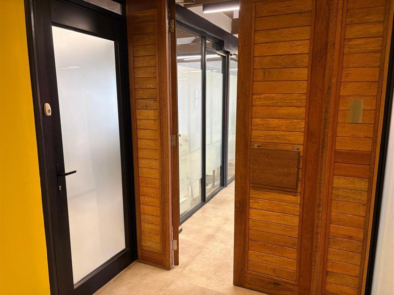 A modern office interior featuring timber-clad walls, glass partition doors, and tiled flooring, creating a professional and structured workspace environment.