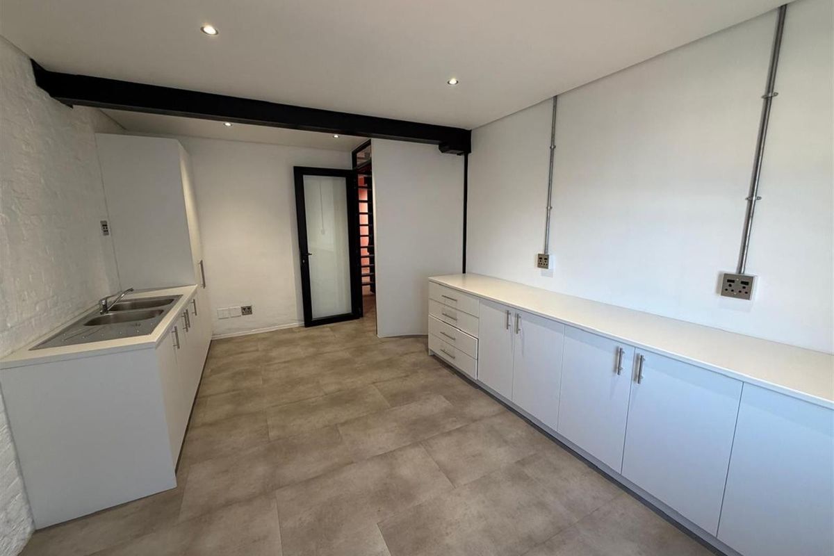 Modern office kitchenette featuring sleek white cabinetry, integrated sink, and durable tiled flooring with exposed structural beam detail.