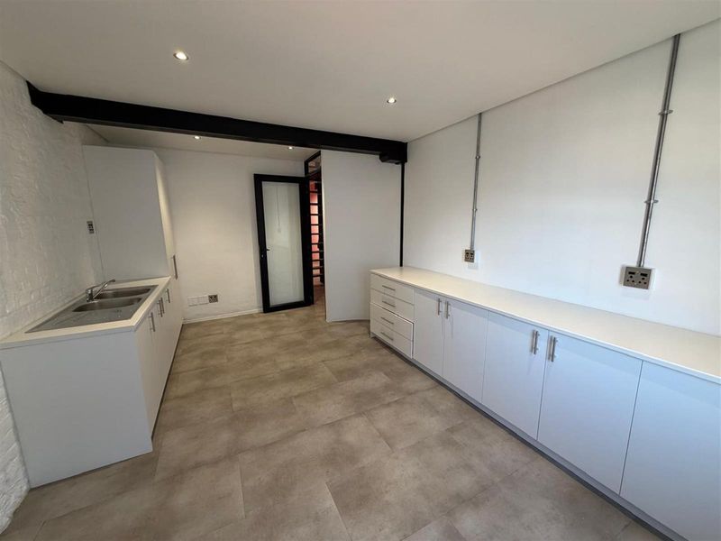 Modern office kitchenette featuring sleek white cabinetry, integrated sink, and durable tiled flooring with exposed structural beam detail.