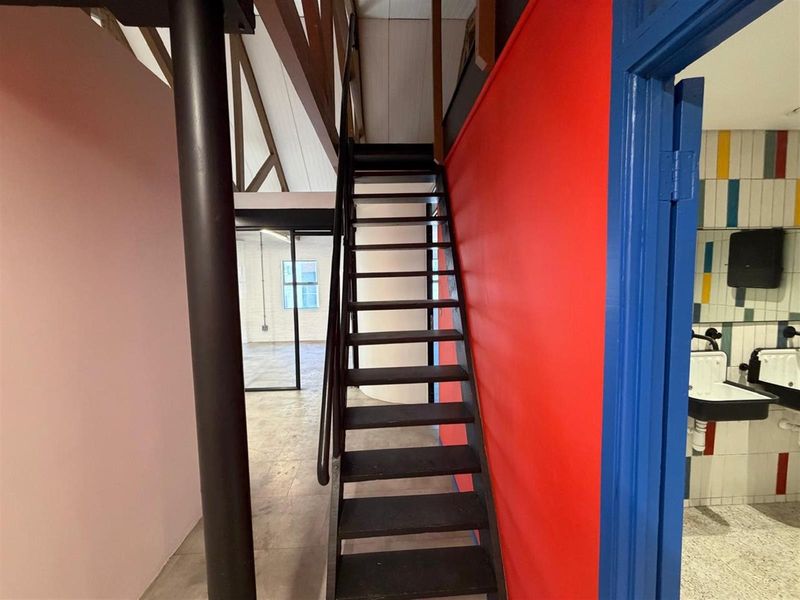 Interior view of an office space featuring a central staircase, exposed roof trusses, and access to a tiled restroom area.