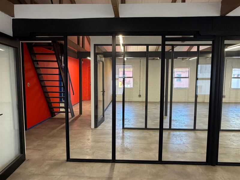 Modern office space featuring industrial-style black steel-framed glass partitions, exposed timber ceiling beams, and polished concrete flooring.