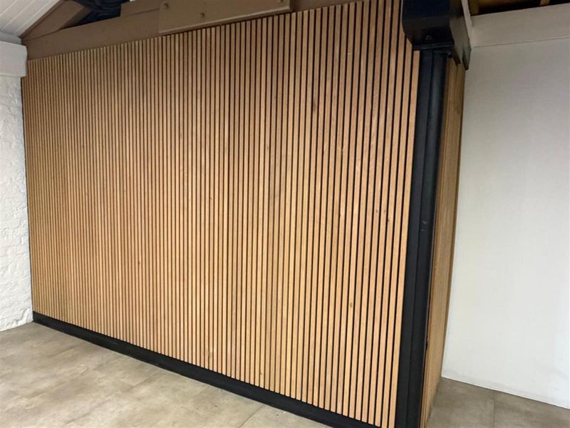 A modern office space featuring a contemporary timber slat feature wall with black trim detailing and neutral floor tiling.