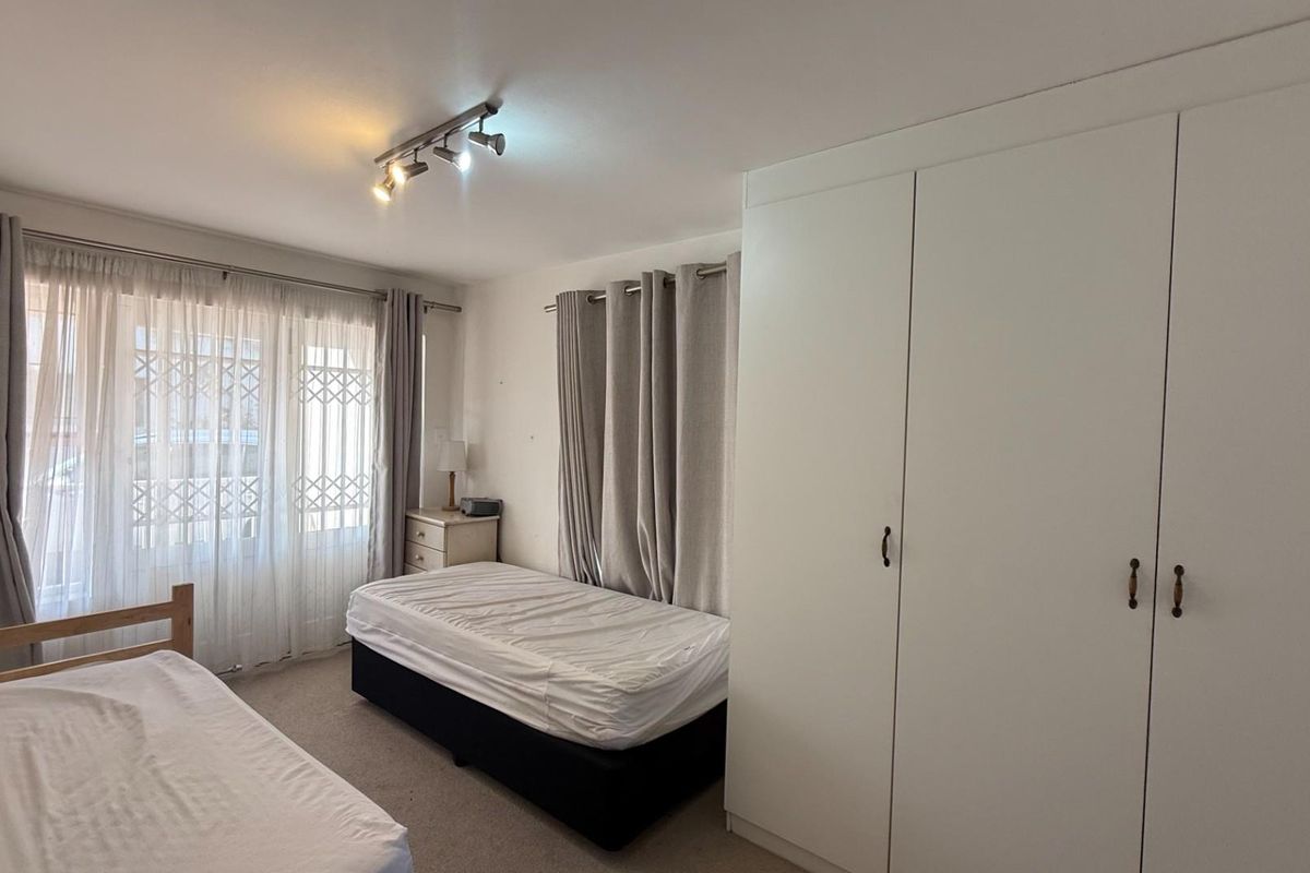 A bedroom featuring built-in white cabinetry, carpeted flooring, and large windows with curtain treatments.