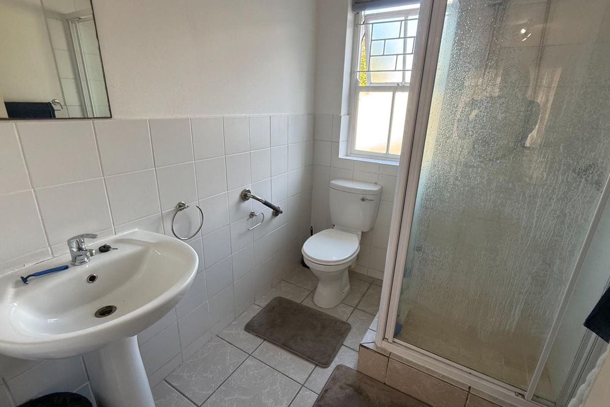 A functional bathroom featuring a pedestal sink, a standard toilet, and a glass-enclosed shower stall with tiled walls and flooring.