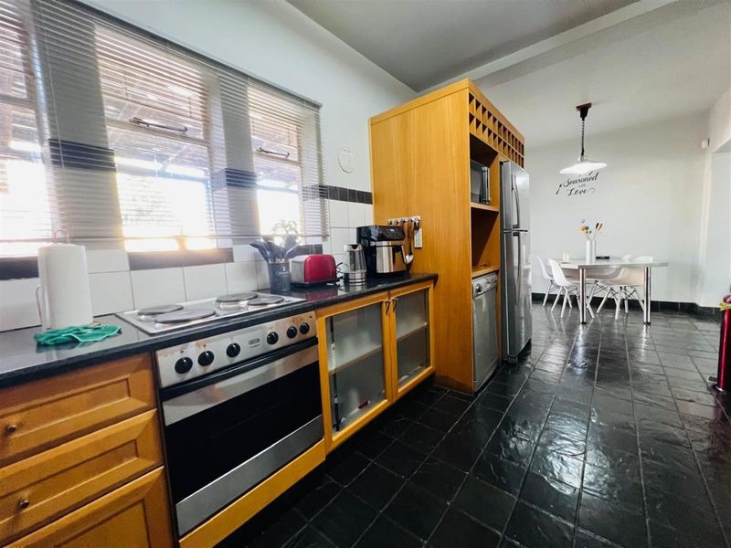 Open-plan kitchen and dining area featuring wooden cabinetry, a built-in oven with hob, and dark tiled flooring.