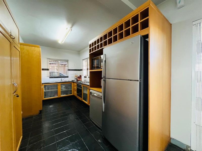 A functional kitchen featuring wooden cabinetry, built-in oven, hob, and dark tiled flooring, offering a practical layout for daily meal preparation.
