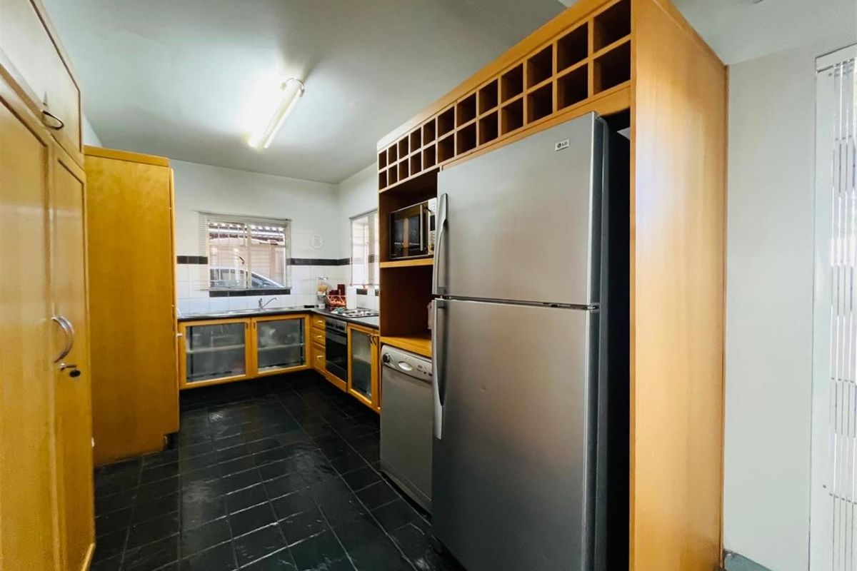 A functional kitchen featuring wooden cabinetry, built-in oven, hob, and dark tiled flooring, offering a practical layout for daily meal preparation.