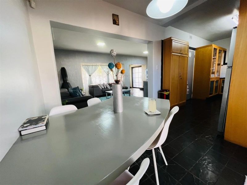 An open-plan living and dining area featuring dark tiled flooring, built-in wooden cabinetry, and a seamless flow between the kitchen and lounge spaces.