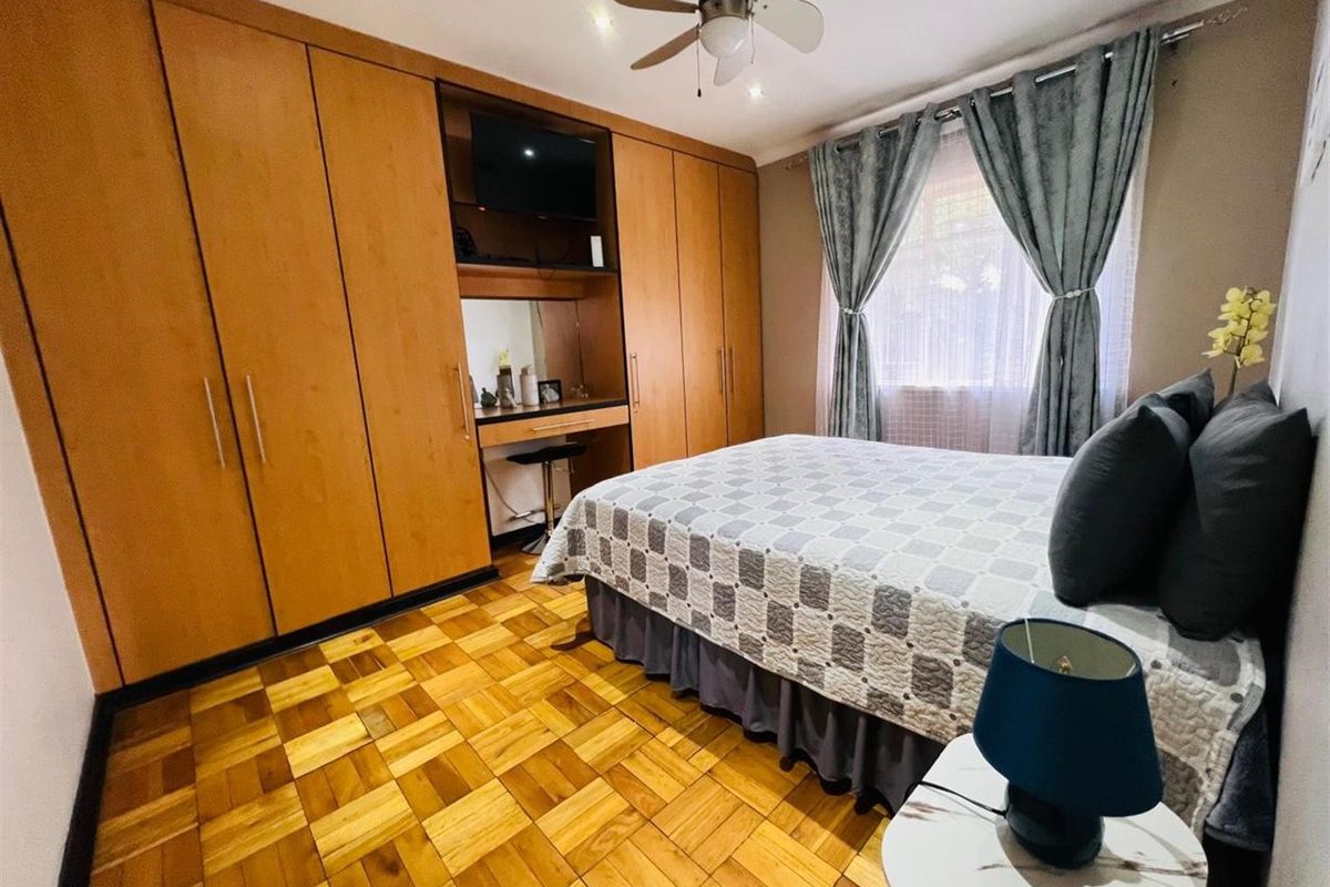 A well-maintained bedroom featuring warm parquet flooring, extensive built-in wooden cabinetry with an integrated vanity, and a ceiling fan.