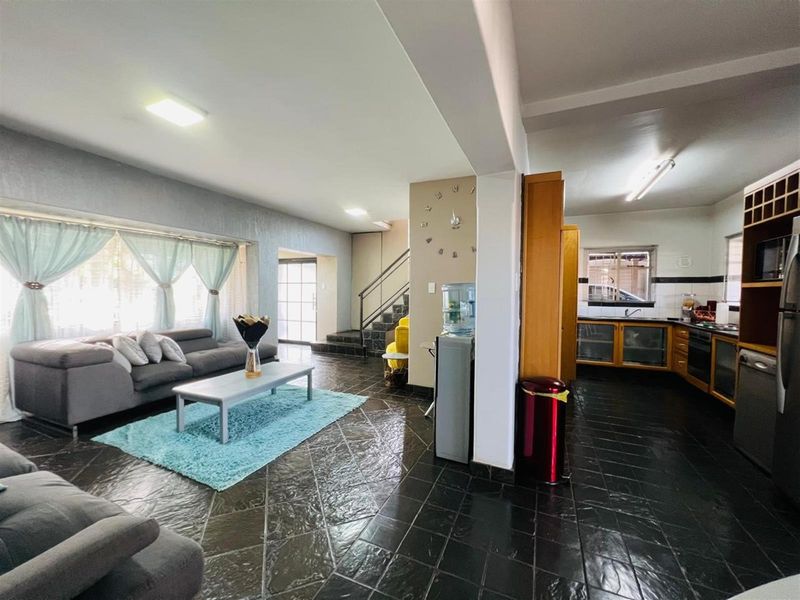 Open-plan living area featuring dark tiled flooring, a functional kitchen with wooden cabinetry, and a staircase leading to the upper level.