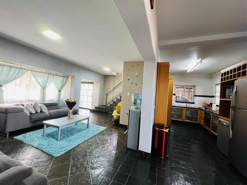 Open-plan living area featuring dark tiled flooring, a functional kitchen with wooden cabinetry, and a staircase leading to the upper level.