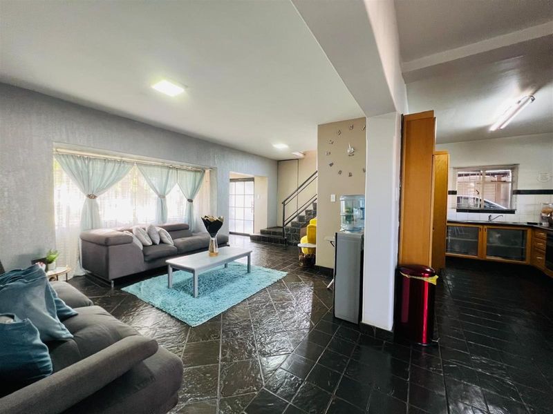 An open-plan living area featuring dark tiled flooring, a staircase, and an adjacent kitchen space with built-in cabinetry.