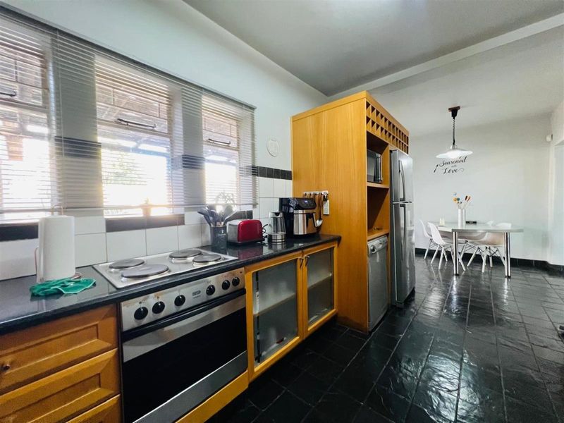 Open-plan kitchen featuring wooden cabinetry, dark stone countertops, a built-in oven with electric hob, and tiled flooring, flowing into a dining area.