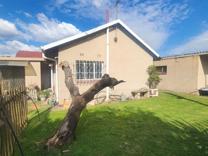 Rear view of the house featuring a lawned garden area, security bars on windows, and a covered patio section.