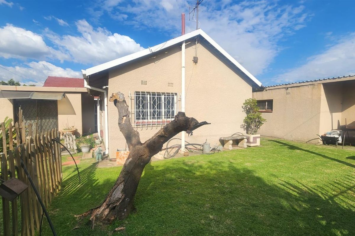 Rear view of the house featuring a lawned garden area, security bars on windows, and a covered patio section.