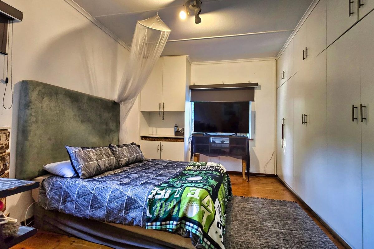 A functional bedroom featuring extensive built-in cabinetry, hardwood flooring, and roller blinds, offering ample storage and a comfortable living space.