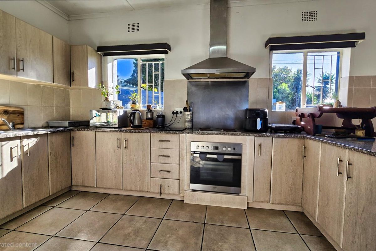 A functional kitchen featuring light wood-finish cabinetry, granite countertops, tiled flooring, and built-in stainless steel appliances including an oven and extractor fan.