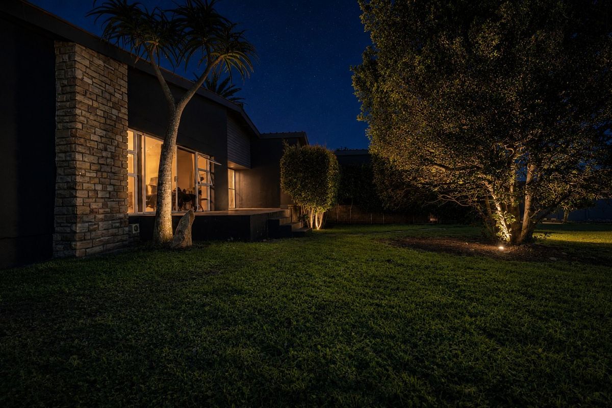 Night view of the rear exterior featuring stone cladding, sliding glass doors, and illuminated garden landscaping.