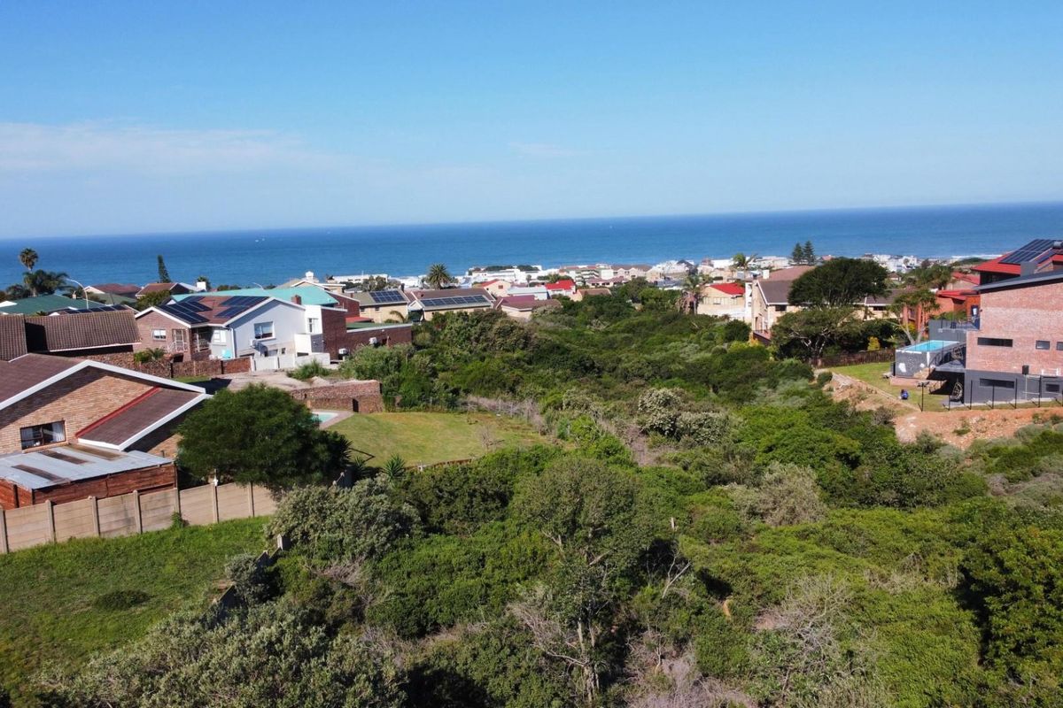 An elevated aerial view of a vacant residential plot surrounded by established coastal neighborhood homes with ocean views.