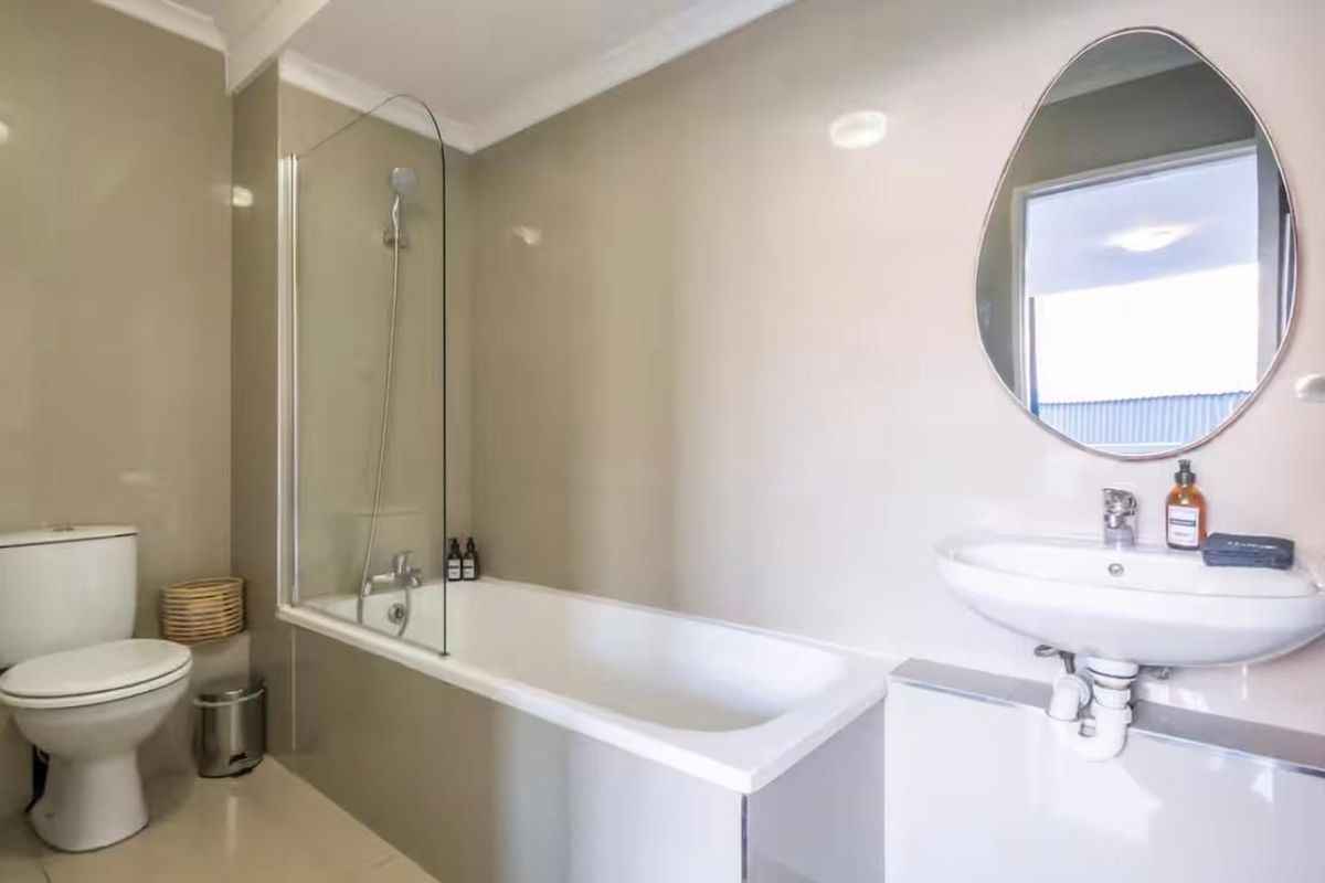 A clean, modern bathroom featuring a white bathtub with a glass shower screen, a wall-mounted basin, and a toilet.