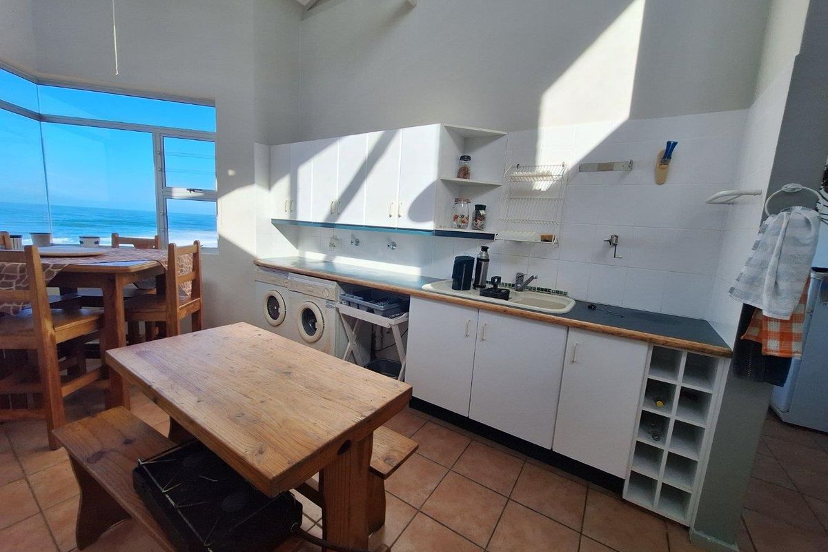 A functional kitchen and dining area featuring white cabinetry, tiled flooring, and large windows offering expansive ocean views.