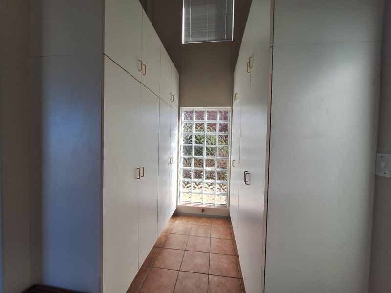 A functional walk-in closet or dressing area featuring extensive floor-to-ceiling built-in cabinetry and a glass block window for natural light.