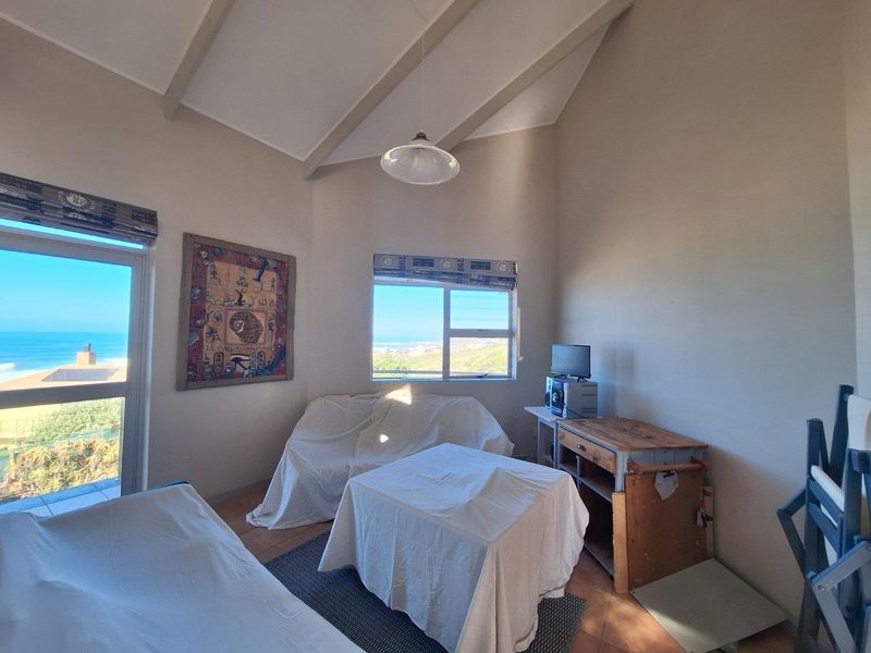 A living area featuring high vaulted ceilings with exposed beams, tiled flooring, and large windows offering scenic coastal views.