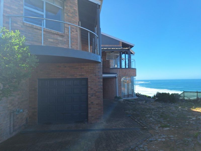A multi-level brick residence featuring a garage, curved balconies with stainless steel railings, and expansive ocean views from its coastal position.