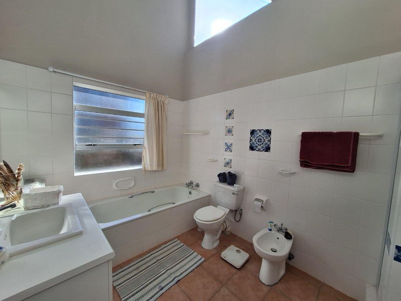 A functional bathroom featuring a built-in bathtub, toilet, bidet, and vanity sink with white wall tiling and a vaulted ceiling with a skylight.