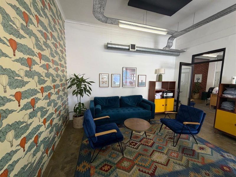 A modern office lounge area featuring exposed industrial ducting, polished concrete flooring, and a decorative feature wall with hot air balloon wallpaper.