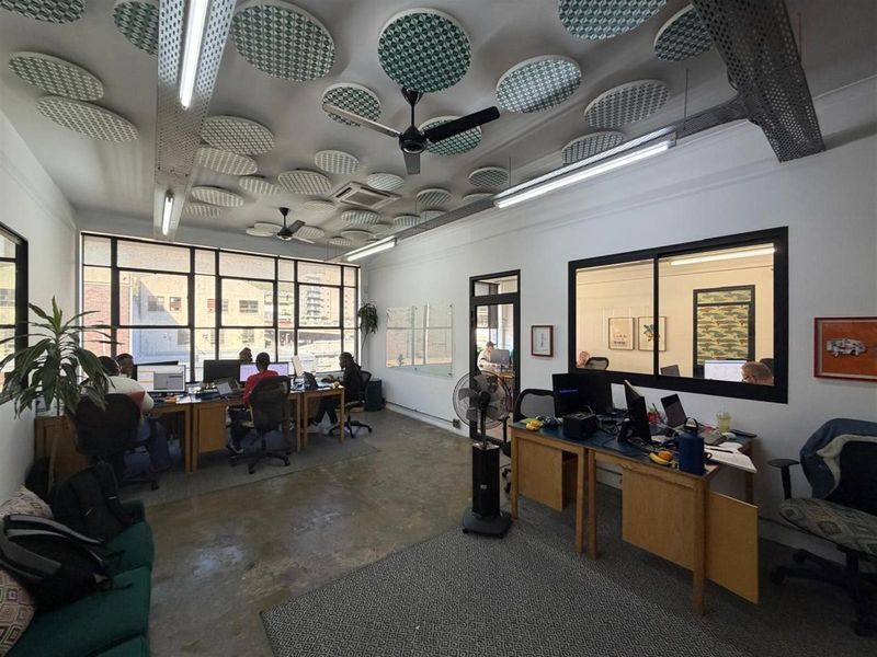 Open-plan office space featuring industrial-style concrete flooring, large windows for natural light, and decorative acoustic ceiling panels.