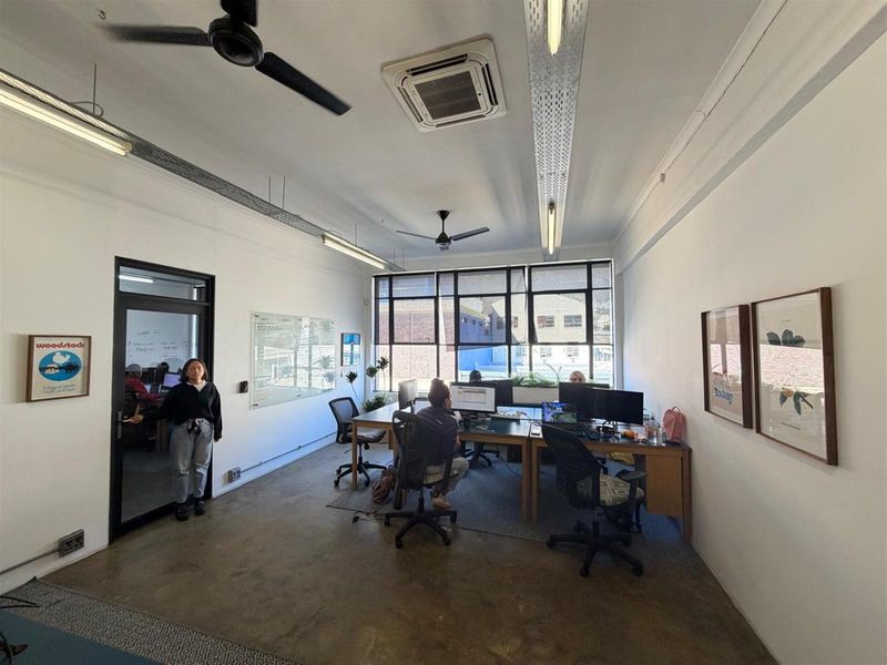 A bright, open-plan office space featuring polished concrete floors, large windows, ceiling-mounted cassette air conditioning, and industrial-style linear lighting.