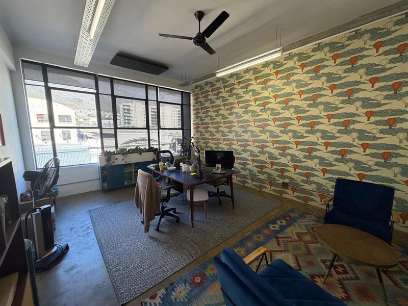 A bright office space featuring large industrial-style windows, polished concrete flooring, a ceiling fan, and a decorative feature wall.