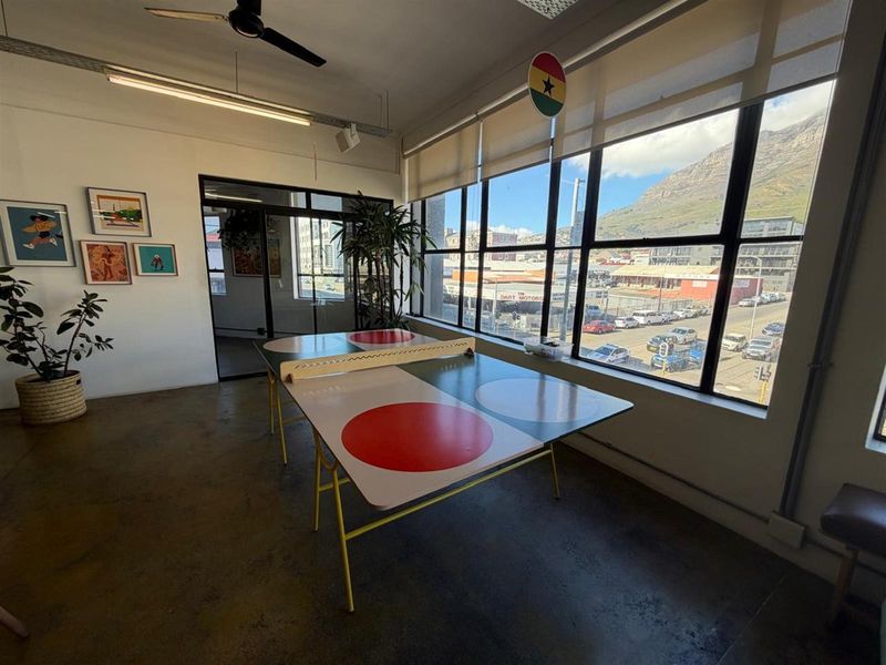 A bright office space featuring polished concrete floors, large industrial-style windows with mountain views, and a ceiling-mounted fan.