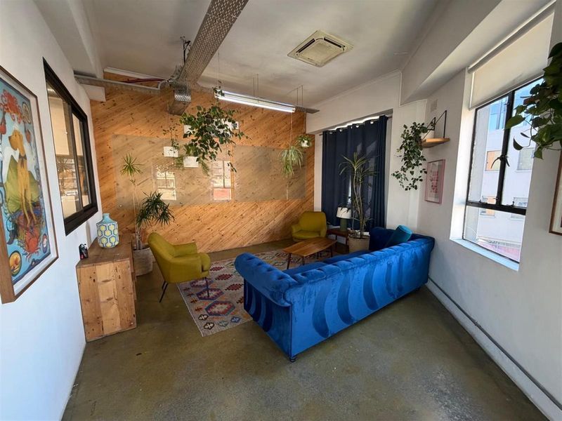 A modern office lounge area featuring industrial-style exposed ceiling ducting, a decorative wood-paneled feature wall, and large windows providing natural light.