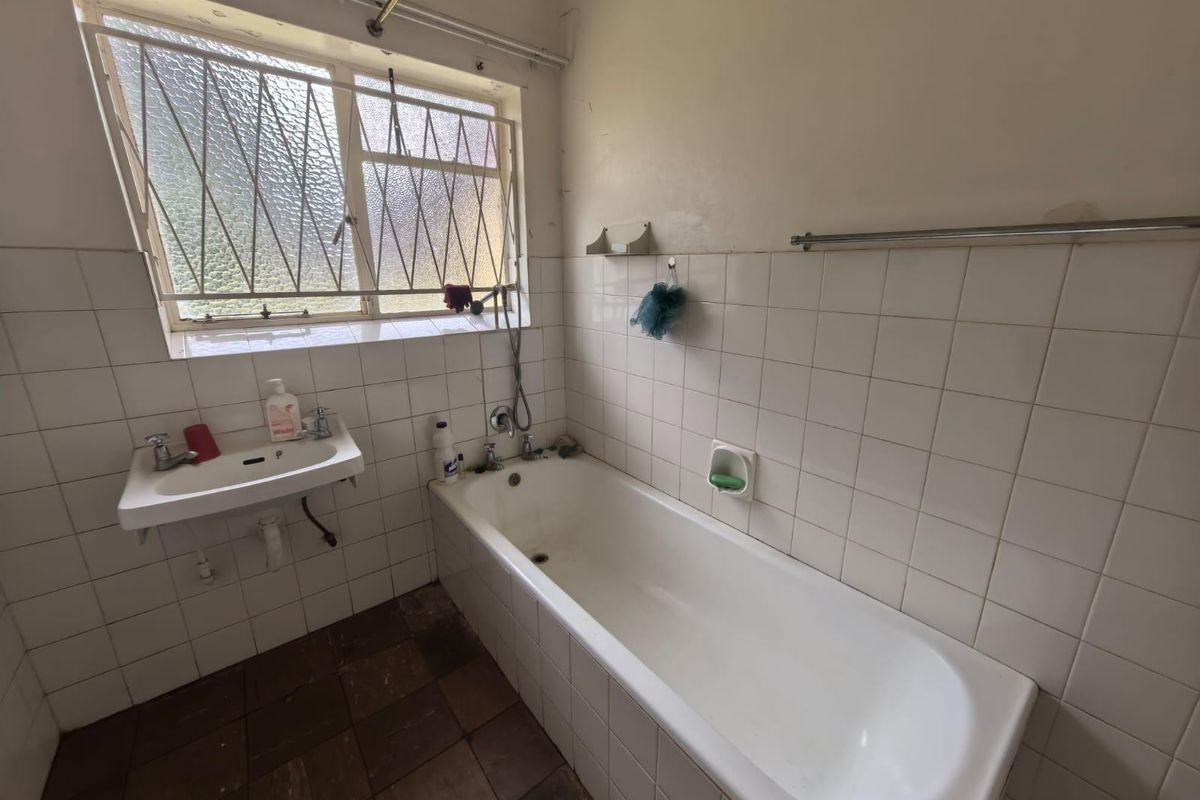 A dated bathroom featuring a standard bathtub, wall-mounted basin, and tiled walls with security bars on the window.