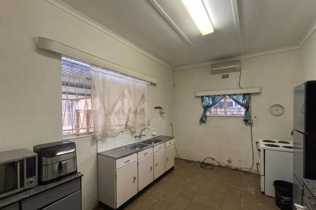 A functional kitchen featuring basic cabinetry, a stainless steel sink, tiled flooring, and a wall-mounted air conditioning unit.