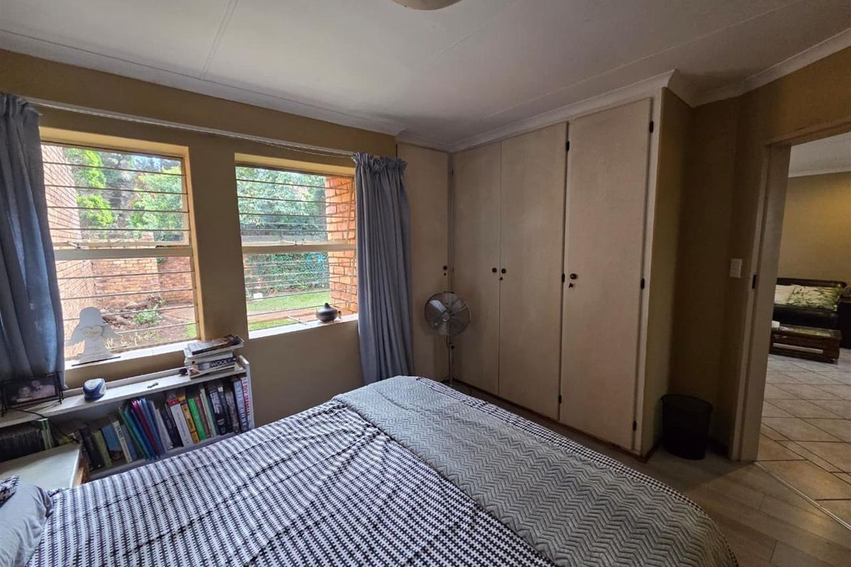 A bedroom featuring built-in cupboards, large windows with security bars, and tiled flooring, offering a functional space with natural light.