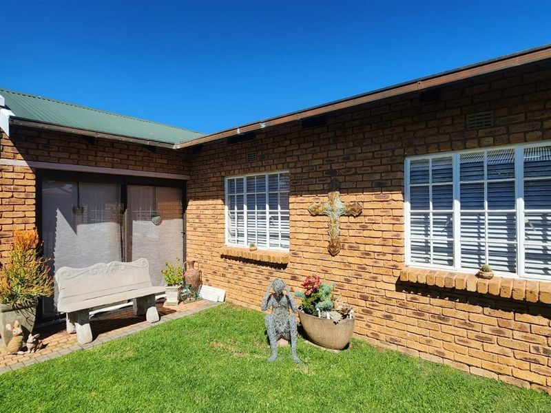 A well-maintained rear exterior view featuring face brick walls, white aluminium window frames, and a paved patio area adjacent to a small garden.