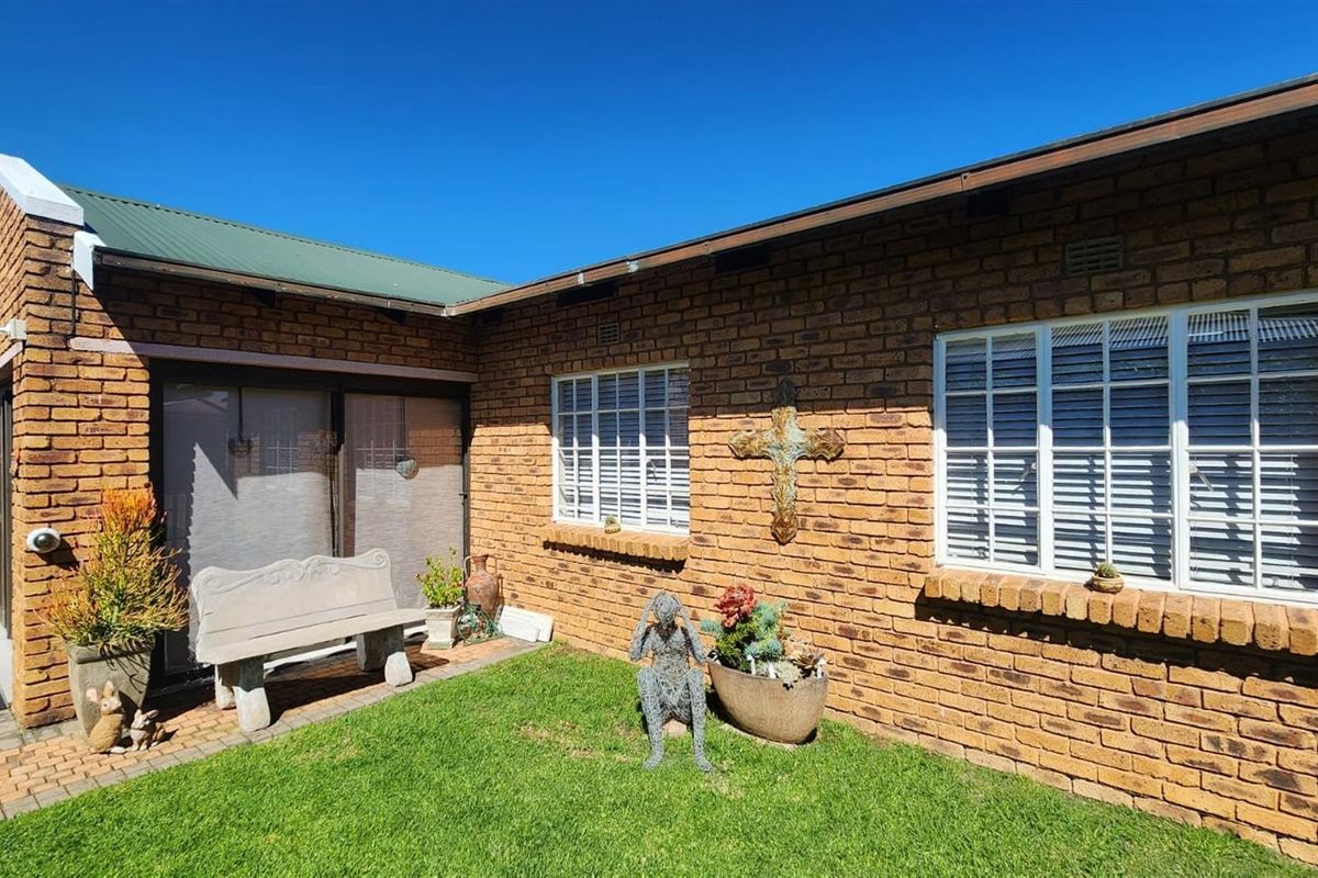 A well-maintained rear exterior view featuring face brick walls, white aluminium window frames, and a paved patio area adjacent to a small garden.
