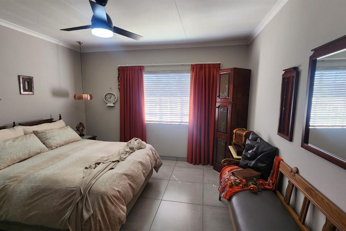 A well-maintained bedroom featuring neutral wall tones, tiled flooring, a modern ceiling fan, and window blinds.