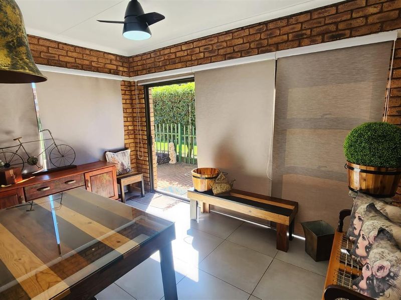 A covered patio area featuring exposed brick walls, tiled flooring, and a ceiling fan, with direct access to the garden.