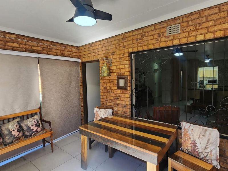 A covered patio area featuring exposed brick walls, tiled flooring, a ceiling fan, and security gate access to the interior living space.
