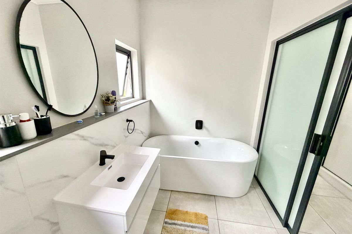 Modern bathroom featuring a sleek freestanding bathtub, wall-mounted vanity with black tapware, and elegant marble-look wall tiling.