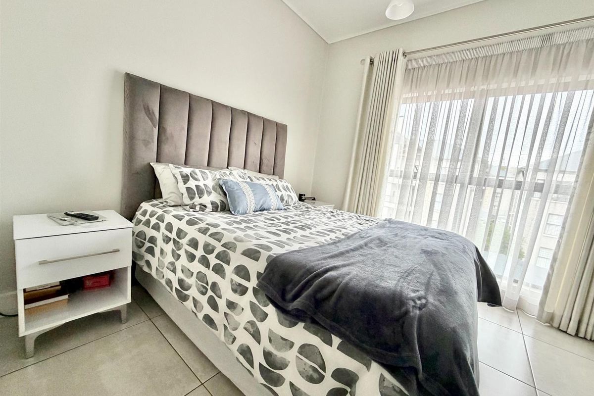 A bright bedroom featuring neutral tiled flooring and a large sliding glass door with curtain tracks, providing ample natural light.