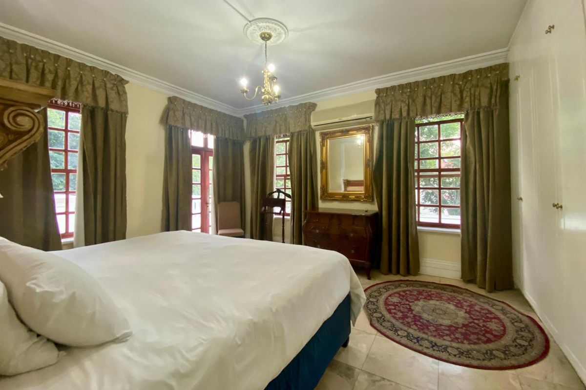 Spacious bedroom featuring tiled flooring, built-in cupboards, crown molding, and multiple windows providing natural light, complemented by a wall-mounted air conditioning unit.